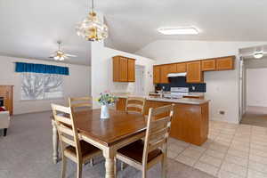 Dining area featuring ceiling fan, light carpet, lofted ceiling, a glass covered fireplace, and a chandelier