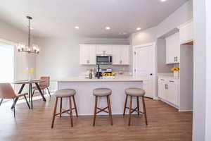 Kitchen with light wood-style floors, a kitchen breakfast bar, stainless steel appliances, a kitchen island with sink, and white cabinetry