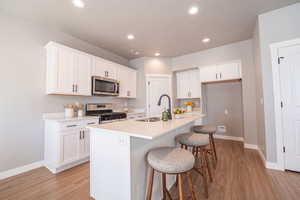 Kitchen with stainless steel appliances, white cabinetry, a breakfast bar area, light wood-type flooring, and recessed lighting