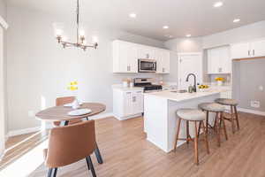 Kitchen with a breakfast bar area, stainless steel appliances, white cabinetry, and light wood-style floors