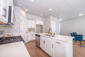 Kitchen with a center island with sink, stainless steel appliances, light wood-type flooring, white cabinetry, and light stone counters