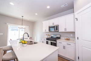 Kitchen with stainless steel appliances, white cabinets, a kitchen island with sink, a breakfast bar, and light wood-style floors
