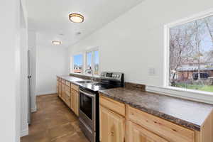 Kitchen with stainless steel electric range oven, dark countertops, and light wood finish cabinets