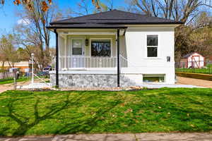 View of front of property featuring covered porch, a front lawn, a shingled roof, and stucco siding