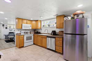 Kitchen featuring stainless steel appliances, recessed lighting, a textured ceiling, wood finish cabinets, and light tile patterned floors