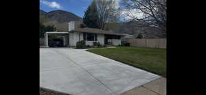 Single story home with a carport, concrete driveway, brick siding, a mountain view, and a chimney