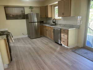 Kitchen with stainless steel appliances, backsplash, light wood finished floors, and light stone counters