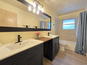 Bathroom featuring double vanity, light wood-style flooring, shower / tub combo, and a textured ceiling