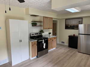 Kitchen with stainless steel appliances, open shelves, a textured ceiling, light wood-type flooring, and decorative backsplash