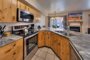 Kitchen with stainless steel appliances, hanging lights, a tiled fireplace, wood finish cabinetry, and open floor plan