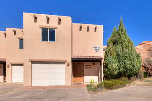 Pueblo-style house featuring an attached garage, stucco siding, driveway, and a tiled roof