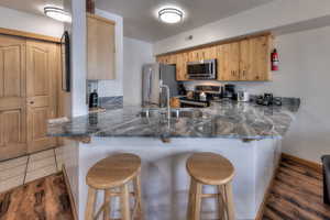 Kitchen with a kitchen bar, dark wood-style flooring, a peninsula, stainless steel appliances, and dark stone counters