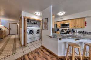 Kitchen featuring a breakfast bar, washing machine and dryer, light wood-style flooring, stainless steel appliances, and a peninsula