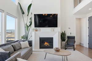 Living area with a high ceiling, a glass covered fireplace, and wood finished floors