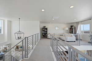 Corridor featuring light carpet, an upstairs landing, and suspended lighting