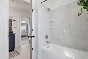 Full bath featuring washtub / shower combination, vanity, connected bathroom, and light marble finish floors