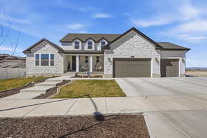 View of front facade featuring stone siding, a porch, an attached garage, concrete driveway, and a front yard