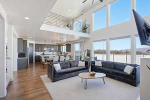 Living area featuring light wood finished floors, ceiling fan, suspended lighting, and a high ceiling