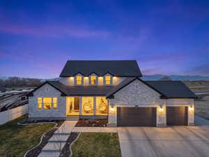 View of front of property featuring a garage, a shingled roof, stone siding, concrete driveway, and covered porch