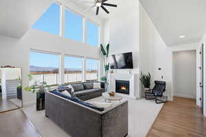 Living area with a lit fireplace, light wood-style floors, a ceiling fan, a high textured ceiling, and recessed lighting