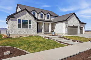 View of front of house featuring covered porch, a garage, a front yard, and stone siding