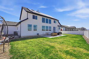 Back of property with a patio, roof mounted solar panels, a trampoline, a fenced backyard, and stucco siding