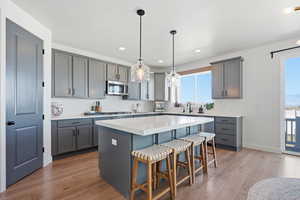 Kitchen with gray cabinets, a kitchen breakfast bar, light wood-type flooring, a kitchen island, and decorative light fixtures