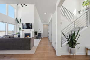 Living area with a lit fireplace, a high ceiling, light wood-type flooring, recessed lighting, and ceiling fan