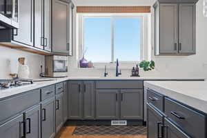Kitchen featuring gray cabinets, stainless steel appliances, light stone counters, and dark wood finished floors