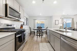 Kitchen with stainless steel appliances, gray cabinets, light wood-style floors, light stone counters, and recessed lighting