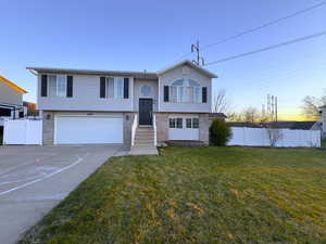 Bi-level home featuring brick and vinyl siding, concrete driveway, an attached garage, and a gate