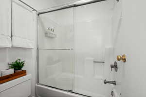 Bathroom featuring toilet and shower / bath combination with glass door