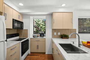 Kitchen with range with electric stovetop, cream cabinetry, freestanding refrigerator, dark wood finished floors, and black microwave