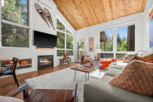 Living area with wood finished floors, a glass covered fireplace, and a vaulted wooden ceiling