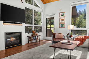 Living room featuring a glass covered fireplace, wood finished floors, a vaulted wood ceiling, and healthy amount of natural light