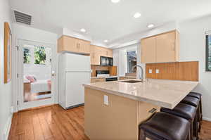 Kitchen with a peninsula, a breakfast bar, freestanding refrigerator, light wood-type flooring, and range with electric cooktop