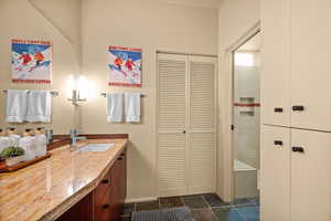 Bathroom with a closet, vanity, dark stone finish flooring, and tiled shower