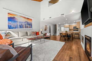 Living area featuring dark wood-type flooring, recessed lighting, a glass covered fireplace, and a high ceiling