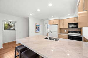 Kitchen with black appliances, a breakfast bar, light wood-style flooring, recessed lighting, and tasteful backsplash
