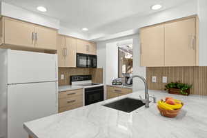 Kitchen with cream cabinets, black appliances, light stone counters, and recessed lighting