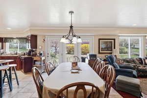 Dining area featuring a textured ceiling, light tile patterned flooring, hanging lights, and crown molding