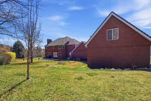 Rear view of house featuring brick siding, a chimney, and a yard