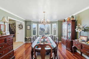Dining room with a chandelier, wood-type flooring, a textured ceiling, and ornamental molding