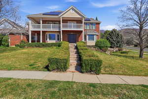 View of front facade featuring roof mounted solar panels, a front yard, and brick siding