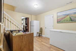 Kitchen with freestanding refrigerator, light wood-style floors, and a textured ceiling