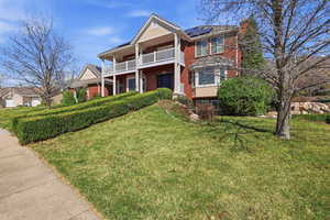 View of front of home with brick siding, a front yard, a porch, roof mounted solar panels, and a chimney