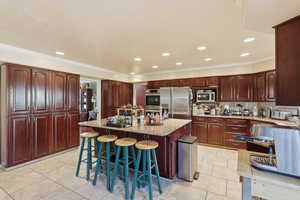 Kitchen featuring a kitchen bar, a kitchen island, light stone counters, light tile patterned floors, and stainless steel appliances