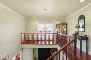 Stairway with suspended lighting, wood finished floors, and crown molding
