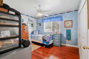 Bedroom with wallpapered walls, dark wood-style flooring, a ceiling fan, and a closet