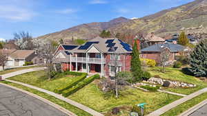 View of front facade with solar panels, brick siding, a mountain view, a front yard, and covered porch